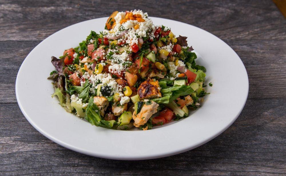 Mediterranean Chicken Salad · Grilled chopped all-natural chicken breast, roasted bell peppers, cucumbers, taboule, seasonal mixed greens, corn, diced tomatoes, red onions, feta, golden raisins, toasted pine nuts, cilantro and lemon vinaigrette.