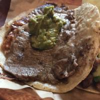 The Rib Eye Taco · Thin sliced griddled rib eye, toasted cheese, refried pinto beans, and guacamole on a homema...