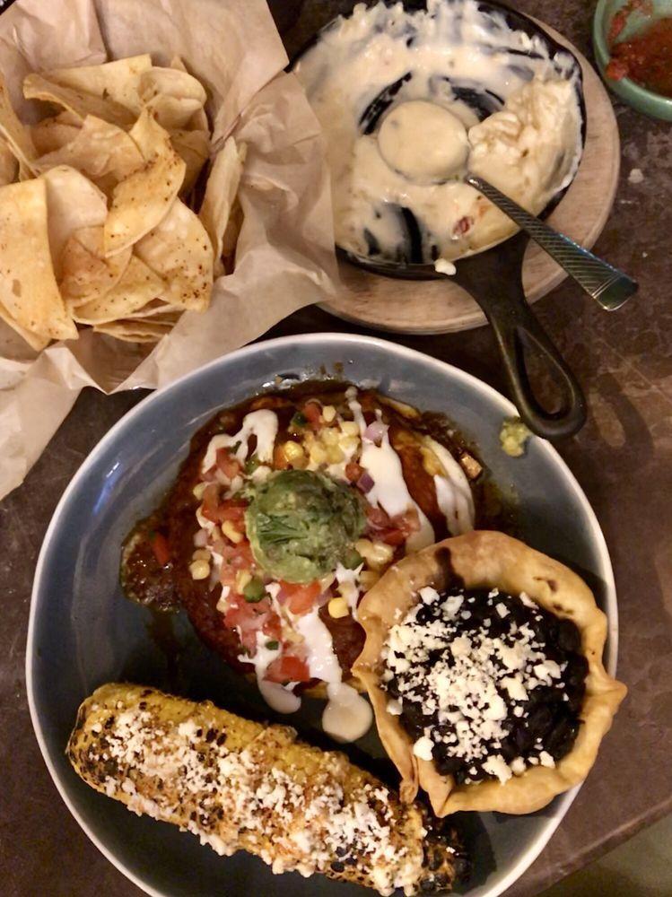 Chicken Enchiladas · Marinated chicken and shredded cheese layered between corn tortillas topped with guacamole, sour cream and corn relish. Served with Mexican rice and elote (Mexican street corn - roasted corn on the cob, chipotle aioli, cilantro and chili powder).