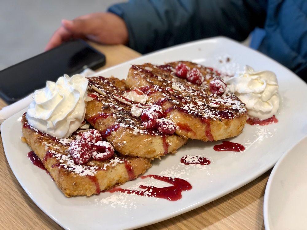 Crunchy French Toast · 3 extra-thick slices of bread rolled in crunchy froasted flakes, sprinkled with almonds, raspberries and powdered sugar. Topped with whipped cream and raspberry drizzle.