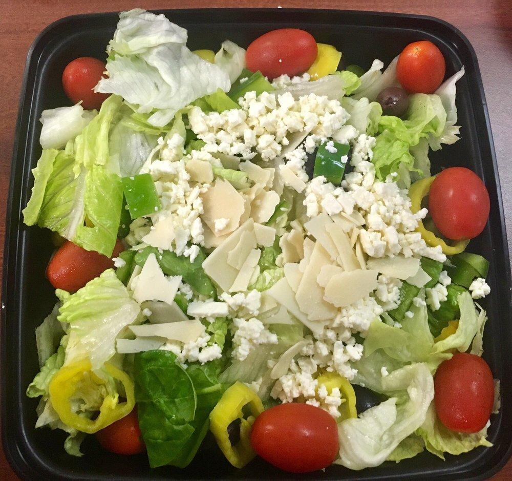 Greek Salad · Romaine and iceberg lettuce, spinach leaves, feta cheese, green peppers, Greek olives, banana peppers, cucumbers, grape tomatoes and shaved asiago cheese.