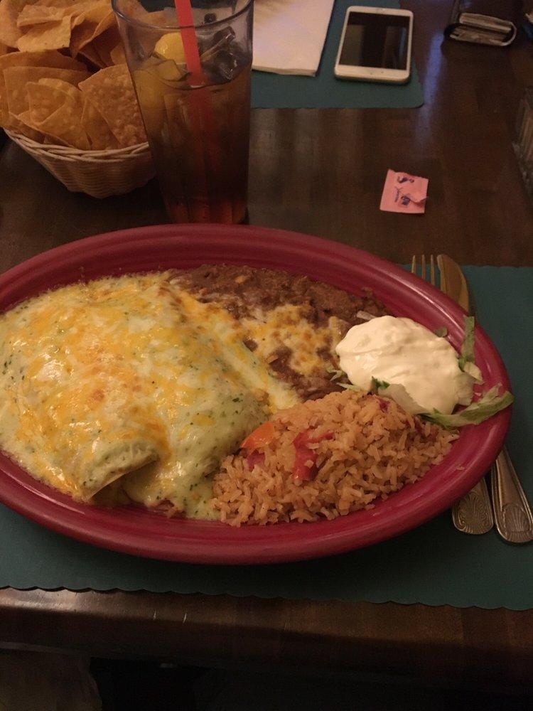 Tomatillo Chicken Enchiladas · 2 enchiladas stuffed with chicken and topped with tangy green tomatillo salsa and Monterrey Jack cheese served with refried beans and rice. Garnished with sour cream and cilantro.