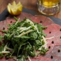 Beef Carpaccio · Thinly-sliced raw beef topped with arugula salad in Italian dressing with Parmesan shavings.
