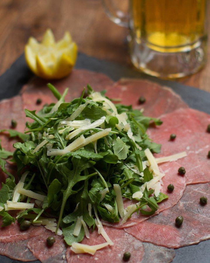 Beef Carpaccio · Thinly-sliced raw beef topped with arugula salad in Italian dressing with Parmesan shavings.