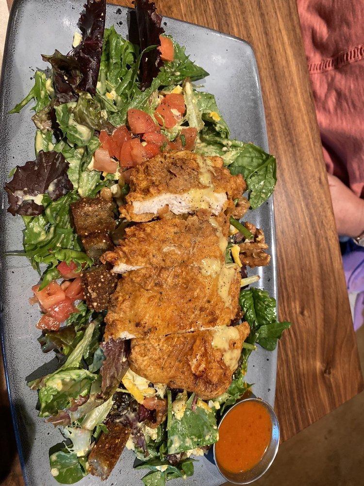 Southern Fried Chicken Salad · Hand-breaded chicken breast on a bed of mixed greens with candied walnuts, housemade indigo cornbread croutons, jack + cheddar cheese, hard-boiled egg, charred sweet corn, tomatoes, honey mustard dressing + a side of our Nashville hot sauce for dipping. 1140 cal.