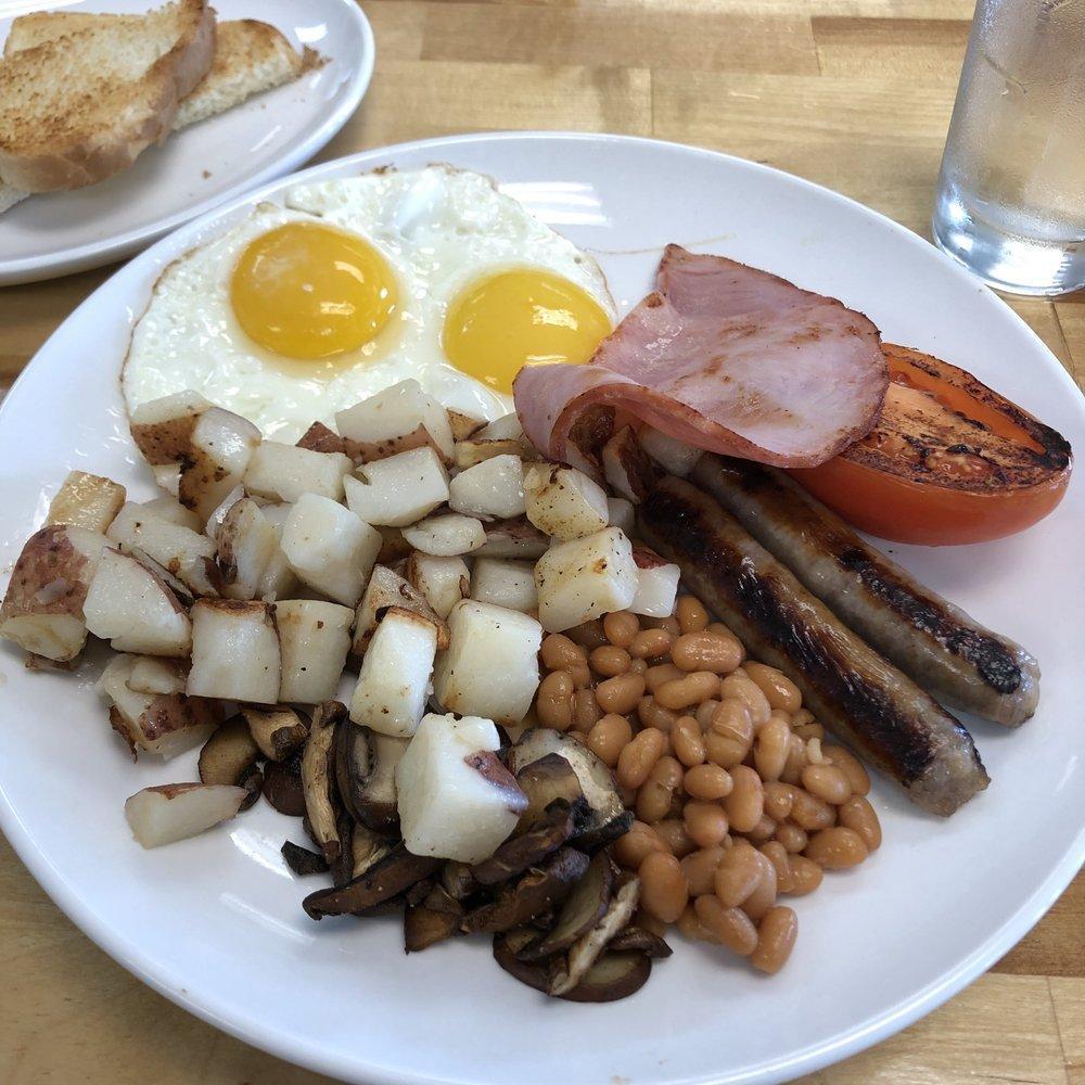 British Breakfast · Two Eggs Any Style, British Banger, Double Smoked Applewood Caramelized Bacon, Grilled Homestyle Potatoes, Roasted Mushrooms, Baked Beans, Grilled Tomatoes served with a side of White Toast