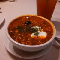 Solyanka · Traditional soup made of smoked meats, garden vegetables, olives, lemon and topped with sour...