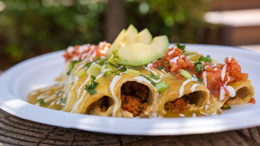Green Chili Enchiladas · Vegan protein beef, zucchini, sauteed peppers and onions wrapped in corn tortillas topped with green chili sauce, vegan con queso, pico de gallo and sliced avocado. Served with mixed greens. Gluten free.