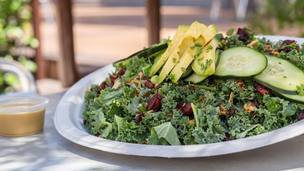 Coconut Kale Salad · Kale, coconut bacon, dried cranberries, cucumbers, scallions and sliced avocado tossed in a light vinaigrette. Gluten free.