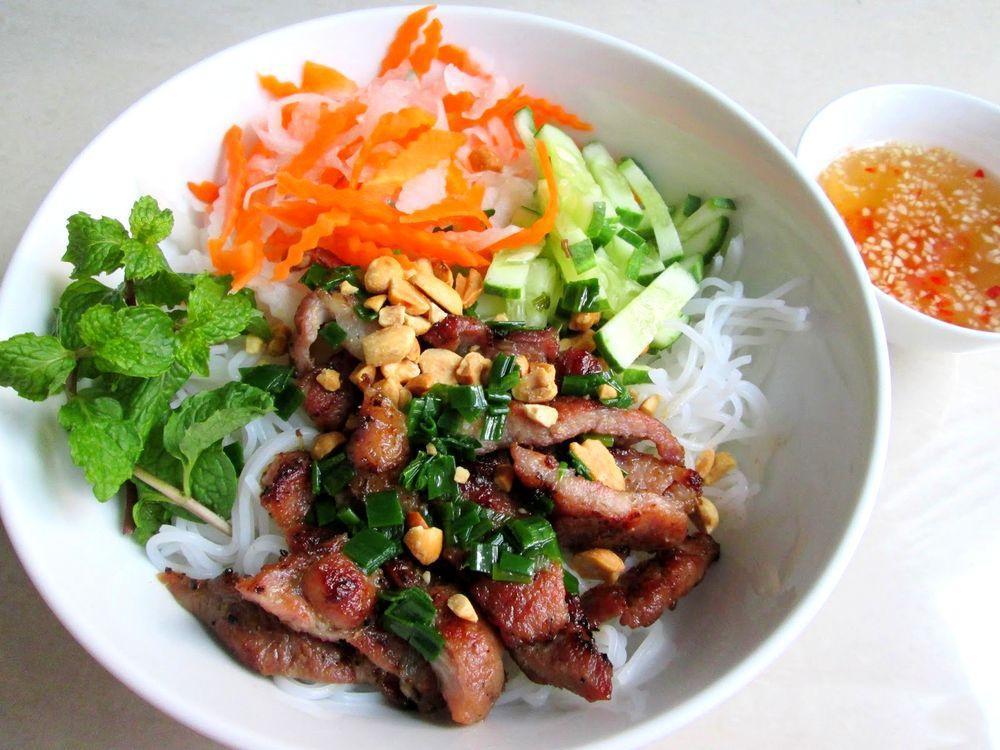 Vietnamese BBQ Pork & Rice Noodle · Vietnamese cold rice vermicelli noodle dish topped with marinated grilled pork, fresh basil and mint, fresh salad, bean sprouts, cucumber and Vietnamese eggs rolls. The dish is dressed in fish sauce & with roasted peanuts, shallots green onions & carrot shavings.