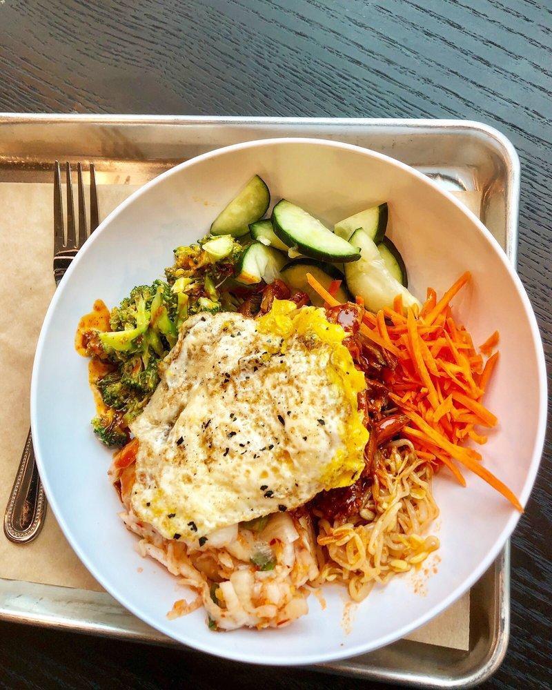 Korean BBQ Pork Warm Rice Bowl · Purple rice, kimchi, cucumbers, spicy broccoli, carrots, sriracha sprouts, fried egg, slow-roasted pork. (egg, soy) Suggested with Korean BBQ sauce. (soy)
