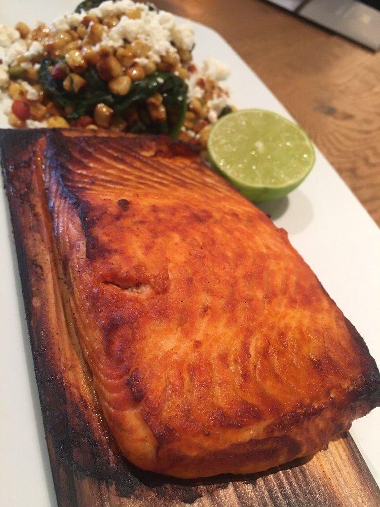 Cedar Plank Salmon · North Atlantic salmon roasted on a cedar plank in our hearth oven with smoked paprika and lime. Served with white corn and spinach succotash topped with feta. Gluten-free ingredients.