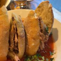Ahogada Torta · Golden pork carnitas, black beans, tomato arbol chile broth, pickled onions. From the woodbu...