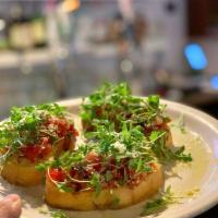Bruschetta · Homemade crostini topped with chopped tomato confit, micro herbs and Parmesan cheese.