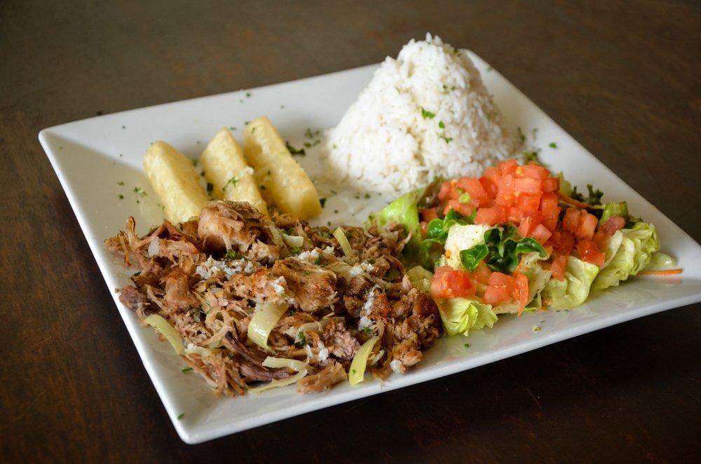 Lechon Asado · Slow roasted pork, marinated in a traditional sour orange mojo. Served with white rice, yuca fries, garlic mojo and salad.
