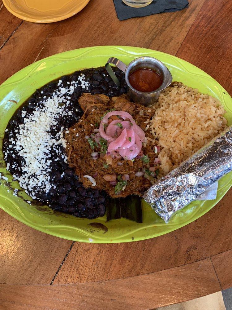 Cochinita Pibil · The Queen's acclaimed pork is marinated in sour orange and achiote paste, wrapped in a banana leaf and slow cooked all night long. Topped with pickled red onions and homemade pico de gallo. Served with fresh hand-pressed corn tortillas, Mexican-style rice and epazote black beans.
