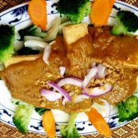 63. Pra Ram Tofu · Fried tofu served on a bed of steamed vegetables, topped with Thai peanut curry sauce. Veget...