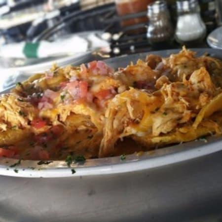 Patacon con Pollo · Fried green plantains layered with chicken fricassee, melted cheese, and topped with fresh tomato salsa.
