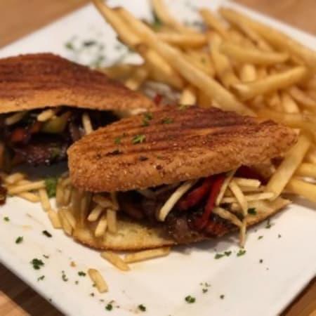 Pan con Bistec Sandwich · Palomilla steak sandwich grilled with onions, peppers, tomatoes and shoestring potato sticks, put together on Cuban bread.