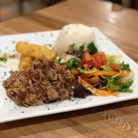 Lechon Asado · Slow roasted pork, marinated in a traditional sour orange mojo. Served with white rice, yuca fries, garlic mojo, and salad.