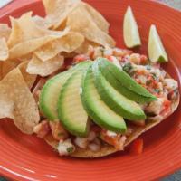 Tostada de Ceviche · Lime marinated fish with tomato, onion and cilantro topped with avocado.