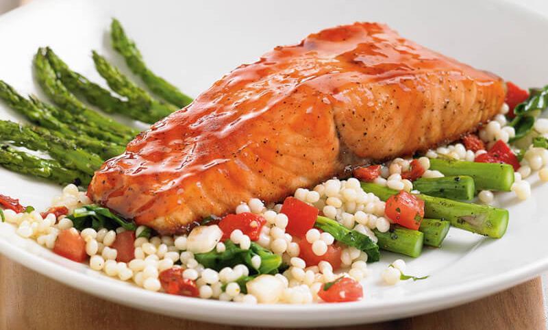 Cherry Chipotle Glazed Salmon* · Oven-roasted atlantic salmon, sweet, savory cherry chipotle glaze, roasted asparagus, fire-roasted red pepper, tomato + spinach couscous