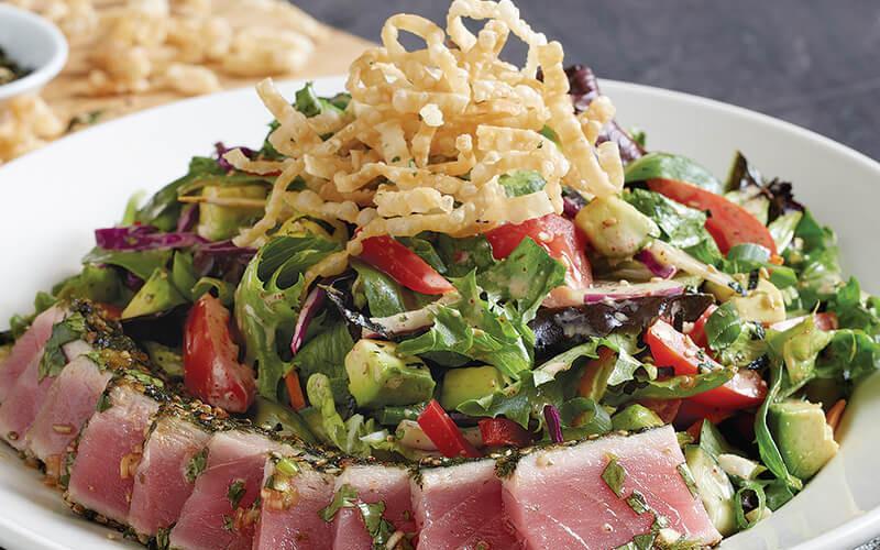 Seared Ahi Salad* · Sashimi-grade ahi, baby field greens, napa cabbage, romaine, red bell peppers, tomatoes, avocado, pickled cucumbers, cilantro, spicy wasabi, crispy wonton strips, red+green onions, rice wine vinaigrette