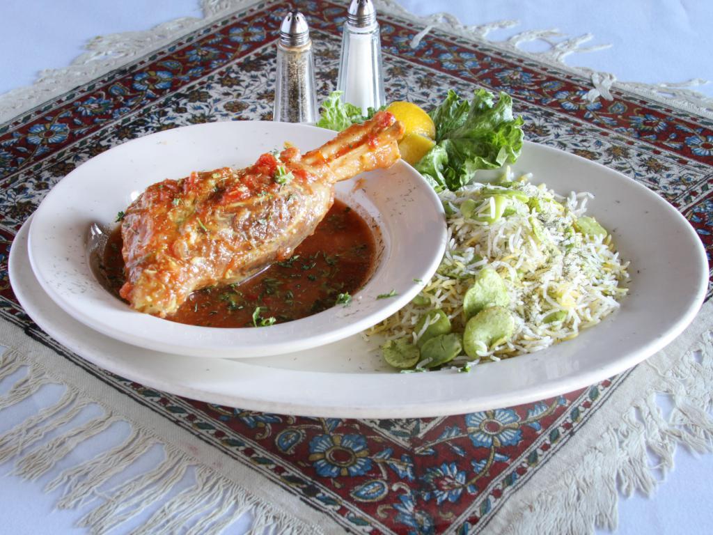 Lamb Shank Mahiche · Lamb shank slowly cooked in tomato sauce with herbs, garlic, and onions. Served with grilled tomato and plan basmati rice chelow.