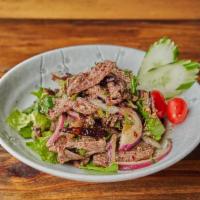 Nuea Yaan Num Tok Salad 🌶 · Marinated grilled beef seasoned with red onion, cilantro, mint leaves, chili and lime juice.
