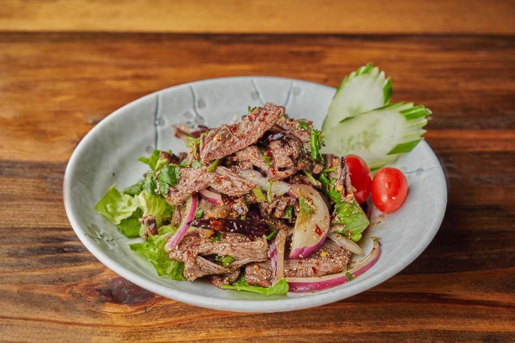 Moo Yaan Num Tok · Marinated grilled pork seasoned with red onions, scallions, mint leaves, grounded roasted rice, chili and lime juice.