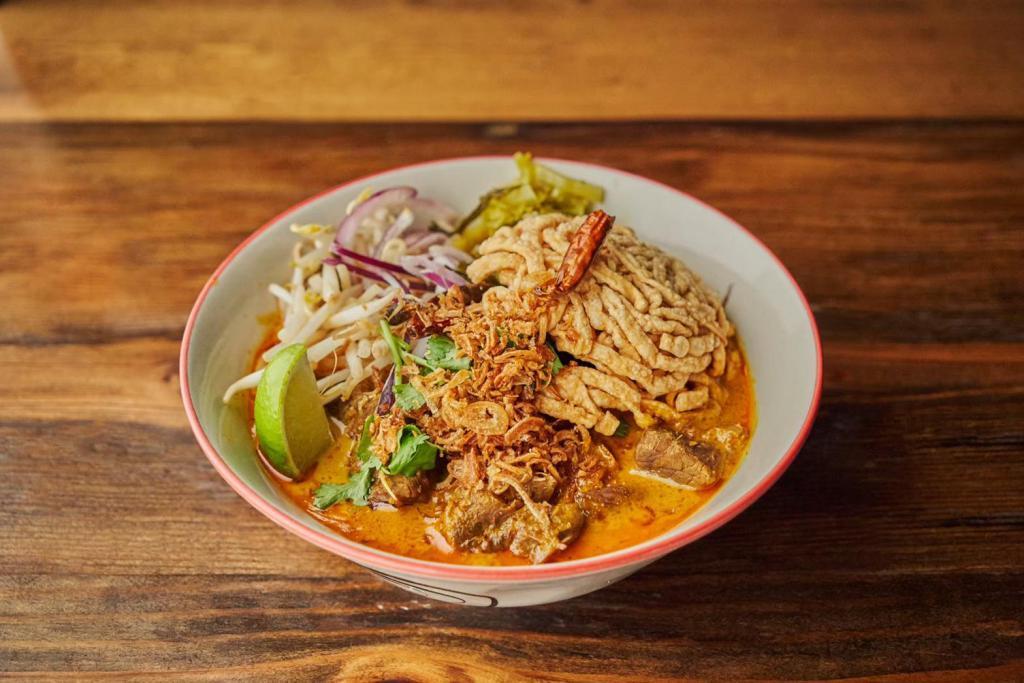 🌶 Khao Soi Stewed Beef · Northern style curry noodle soup with stewed beef, pickle, cilantro, red onion, dried chili, bean sprouts and crispy egg noodles.
