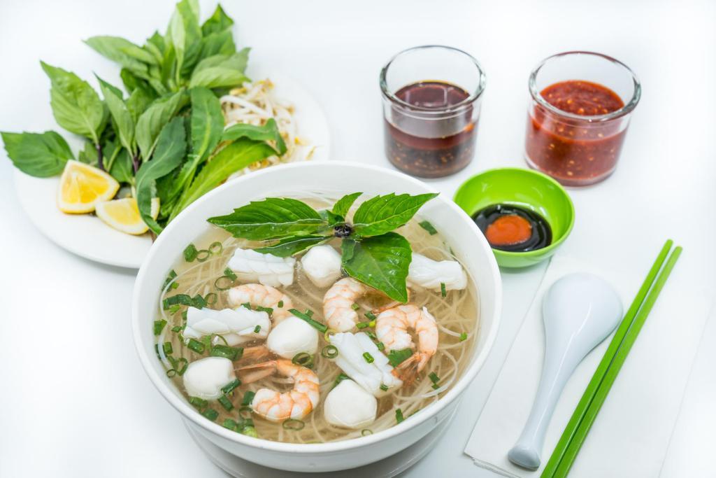 13. Large Seafood Pho Noodle Soup · Vietnamese pho noodle soup served with shrimp, fishcake, and squid, rice noodle, garnished with green and white onion.