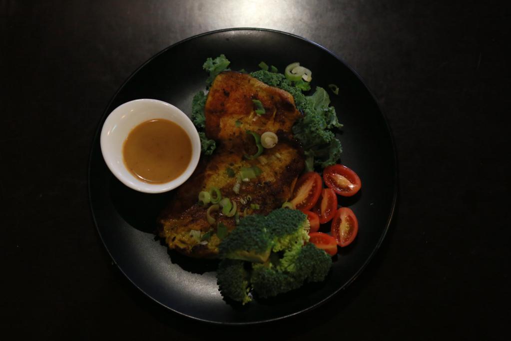 E1. Satay Chicken Steak · Grilled herb-marinated chicken served with kale, broccoli, peanut sauce, and rice on side.