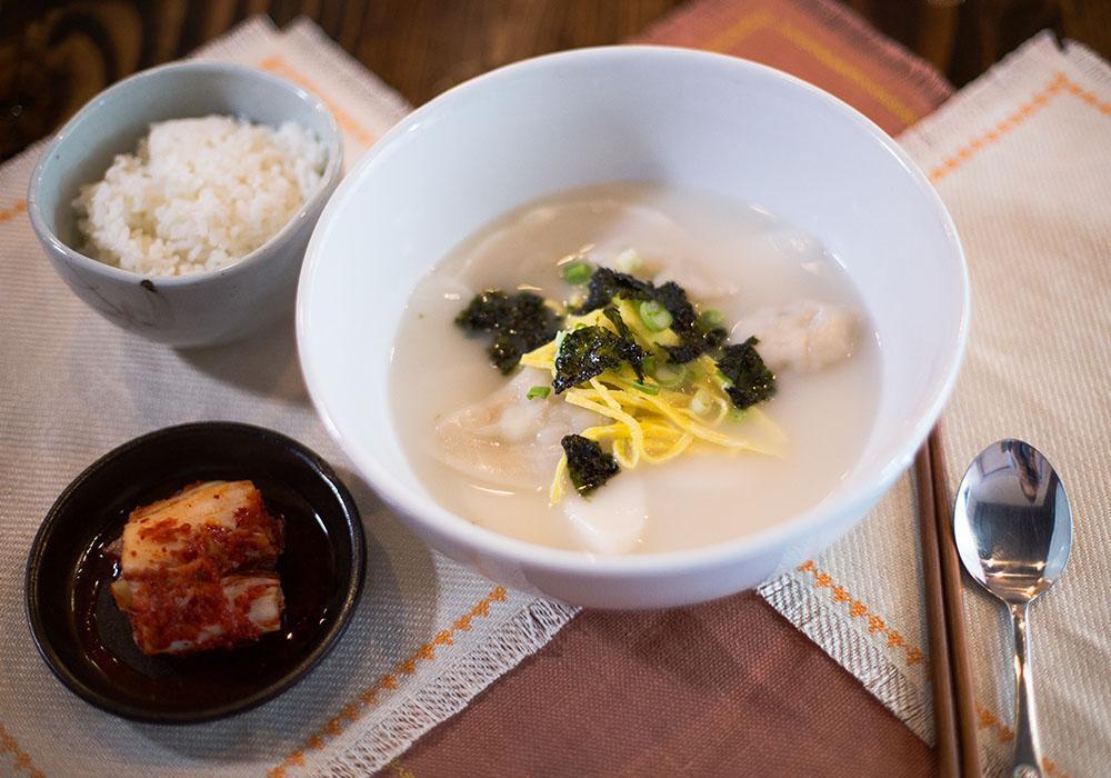 Dumpling Soup · Rice cakes and dumplings in ox bone soup, topped with thinly sliced egg and seaweed flakes.