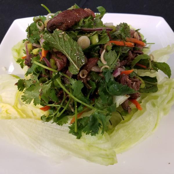 Nua Nam Tok · Grilled steak medium sliced, lemongrass, kefir, mint, cilantro, green and red onions. Rice powder on bed of lettuce.