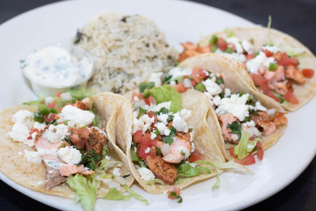 Atlantic Salmon Tacos · Four tacos filled with blackened Atlantic salmon, shredded lettuce, cilantro lime aioli, feta cheese, and pico de gallo. Served with a side of cilantro lime rice.