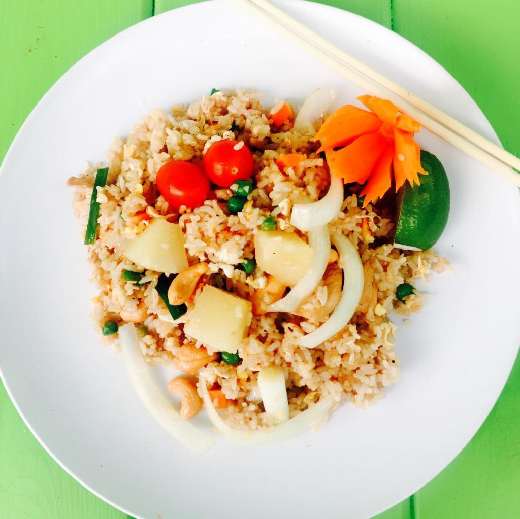 Pineapple Fried Rice · Fried rice with egg, pineapple chunks, onions, green onions, cashew nuts, tomatoes, pea carrots and topped with cilantro cucumber and rime sliced.