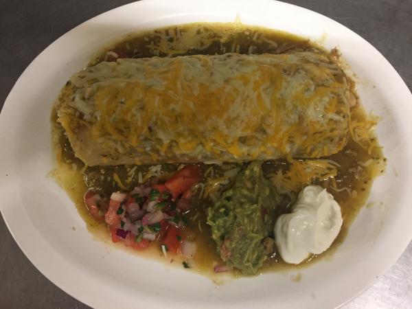 Chile Verde Burrito · Slow cooked pork simmered with roasted tomatillos, jalapenos. Wrapped up with rice and beans. Guacamole, pico and sour cream on the side. Shown with sauce and melted cheese on top.