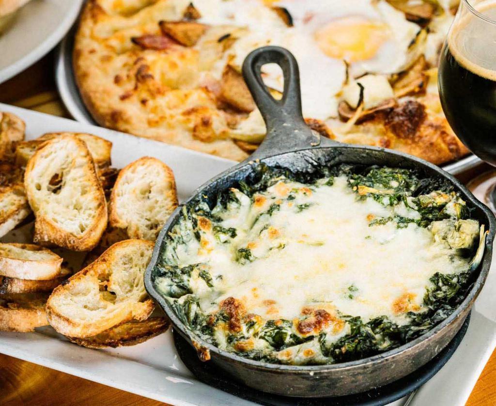Spinach Artichoke Dip · Skillet baked cream cheese dip with fresh saute’ spinach & artichoke hearts. 
 Topped with Mozzarella & Shaved Parmesan Cheese. 
Served with sliced and seasoned fresh baked bread