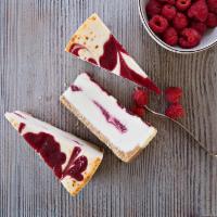 Raspberry White Chocolate Cheesecake · A silken smooth white chocolate cheesecake with vibrant red raspberry swirls all around.