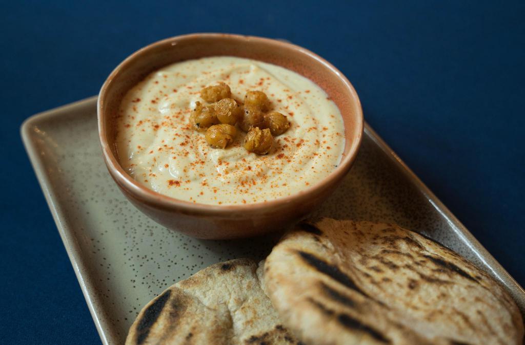 Original Hummus · Made of mashed chick peas, blended with tahini, extra virgin olive oil, topped with roasted garbanzos and paprika. Served with warm pita. (V, GF)