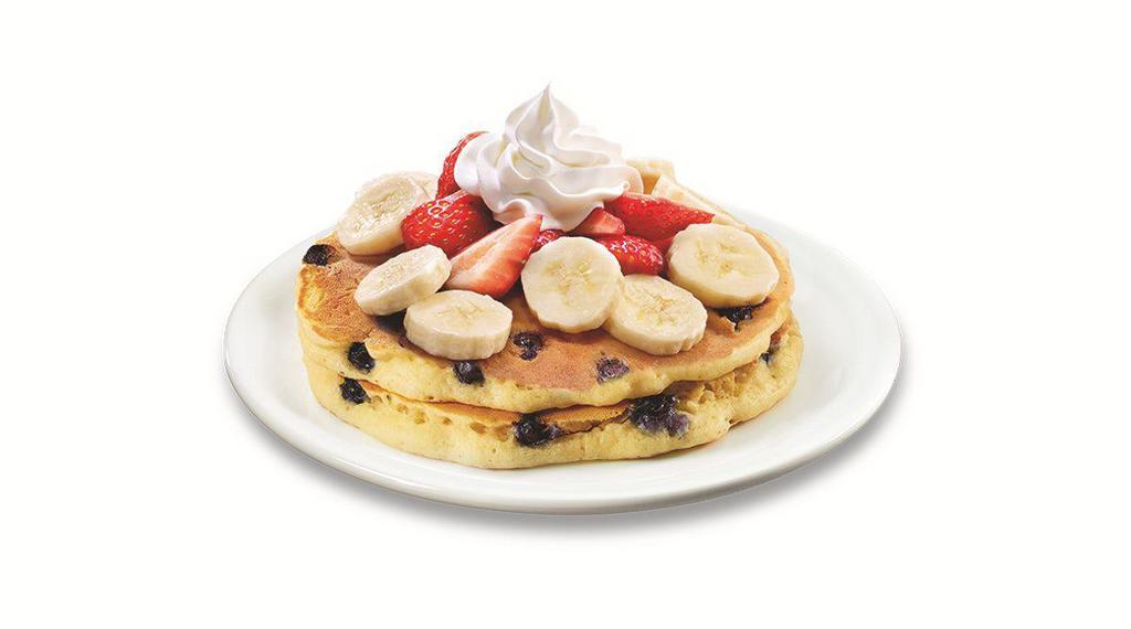 Stack of Double Berry Banana Strawberry Pancakes  · Buttermilk pancakes cooked with blueberries and topped with fresh seasonal berries, bananas and whipped cream. 