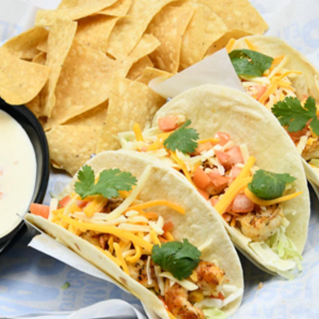 Shrimp Tacos · Blackened shrimp,  with green cabbage, cilantro, tomatoes, shredded cheese, and avocado lime dressing on flour tortilla. Served with queso and tortilla chips.