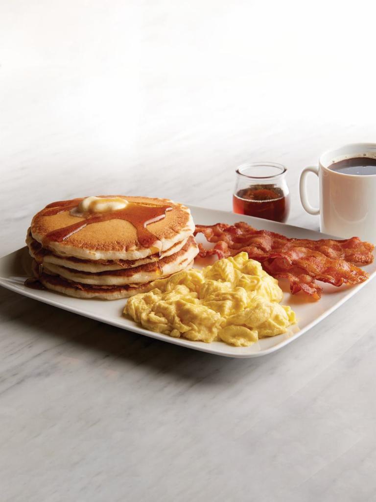 Buttermilk Pancakes with Eggs and Bacon · Four fluffy buttermilk pancakes with butter and vanilla maple syrup. Served with a side of bacon and scrambled eggs.