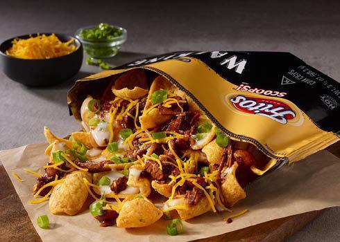 Brisket Chili Walking Taco · Texas-style brisket chili over a bed of Fritos, topped with creamy Poblano Queso, shredded cheddar cheese, and green onions. Built in a walking taco bag for enjoyment at the table or on the go.