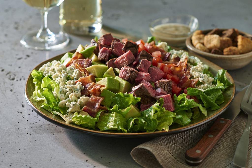 Steakhouse Cobb Salad · Crisp chilled greens tossed with our house vinaigrette and layered with fresh avocado, tomato, applewood-smoked bacon, bleu cheese crumbles, and topped with your choice of protein.