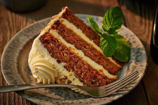 Spiced Carrot Cake · A slice of carrot cake with pineapple and walnuts, a dash of vanilla and cinnamon, layered together with cream cheese frosting. Contains nuts.