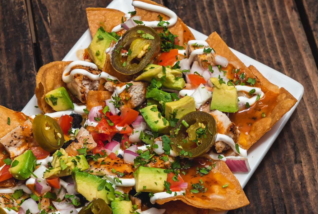 Grilled Chicken Nachos · Black beans, avocado, tomatoes, cilantro, red onions, cheese blend, sliced jalapenos, chipotle sauce and crema.