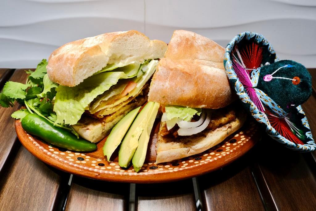 Torta de Milanesa de Pollo · Specialty Sandwich with breaded chicken cutlet with mayo and refried bean spread, queso oaxaca, sliced avocado, tomato, onion, and pickled jalapeños.