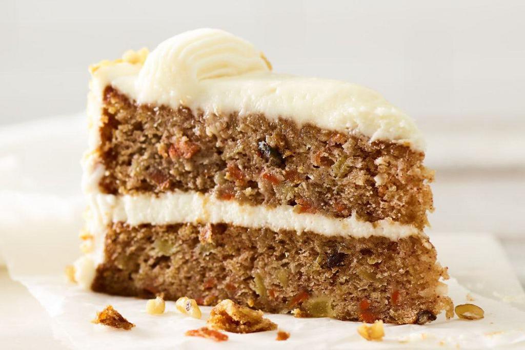 Carrot Cake Slice · Two-layer cake with shredded carrots, pineapple, sweetened coconut and pecan pieces, covered in cream cheese frosting and garnished with walnuts.